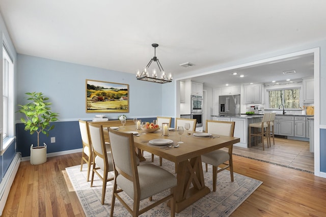 dining room with visible vents, baseboards, baseboard heating, light wood finished floors, and an inviting chandelier