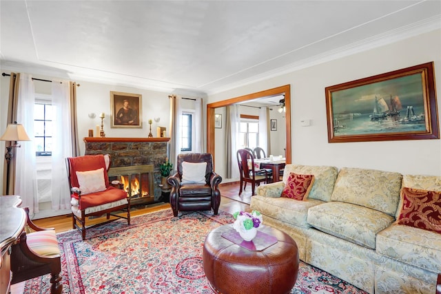 living area with ornamental molding, a stone fireplace, and light wood-style flooring