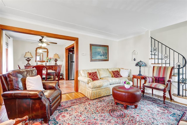 living room with ornamental molding, light wood-type flooring, ceiling fan, and stairway