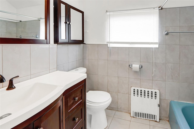 bathroom with radiator, toilet, tile patterned floors, vanity, and tile walls