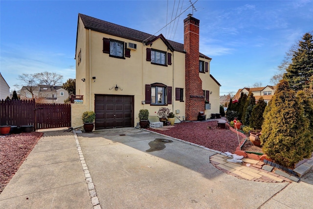 view of front of house with driveway, a garage, a chimney, fence, and stucco siding