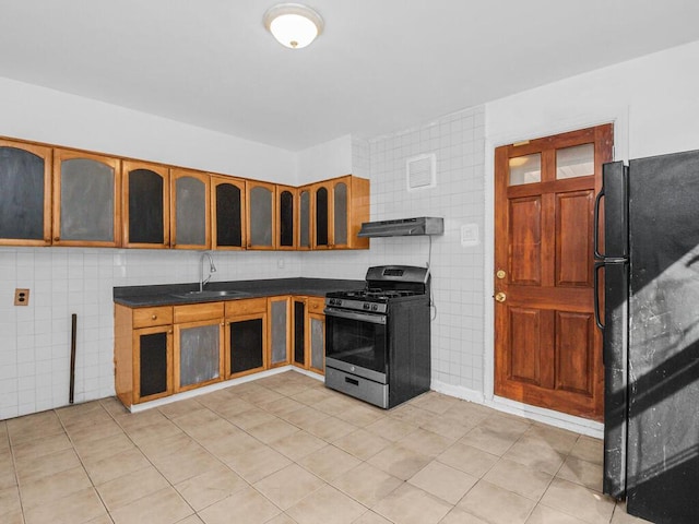 kitchen with stainless steel gas range oven, under cabinet range hood, a sink, freestanding refrigerator, and dark countertops