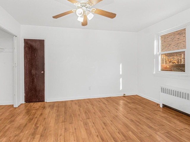 empty room featuring a ceiling fan, light wood-type flooring, radiator, and baseboards