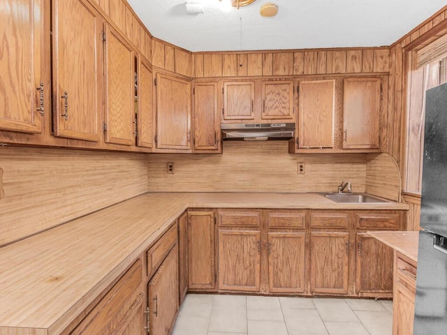 kitchen featuring brown cabinets, light countertops, a sink, and under cabinet range hood