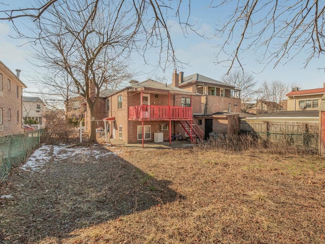 rear view of house with brick siding, a chimney, stairway, a fenced backyard, and a wooden deck