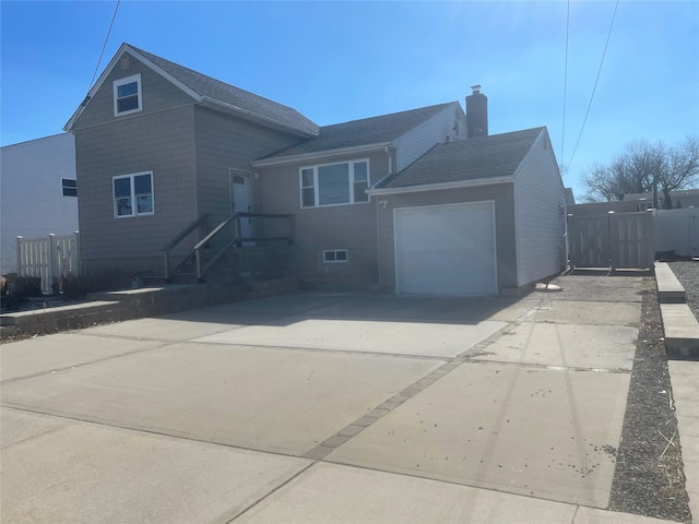 traditional-style home with concrete driveway, fence, a chimney, and an attached garage