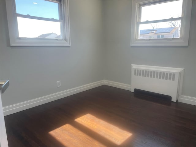 empty room with radiator, baseboards, and dark wood finished floors