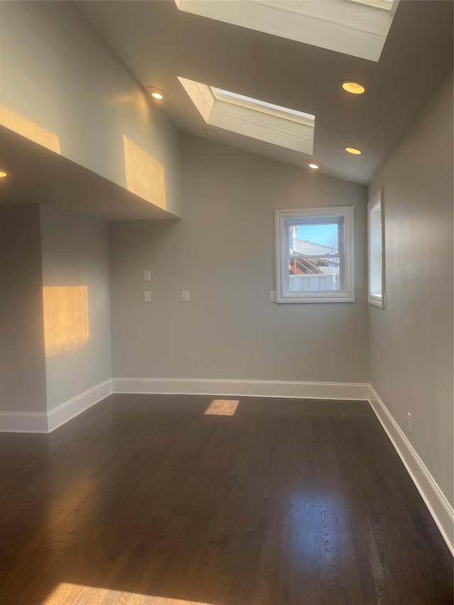 empty room featuring vaulted ceiling with skylight, baseboards, dark wood finished floors, and recessed lighting