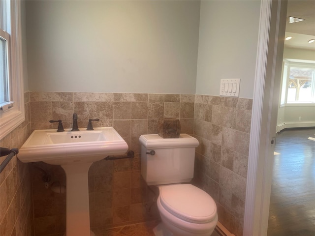 bathroom with a baseboard heating unit, toilet, a wainscoted wall, and tile walls