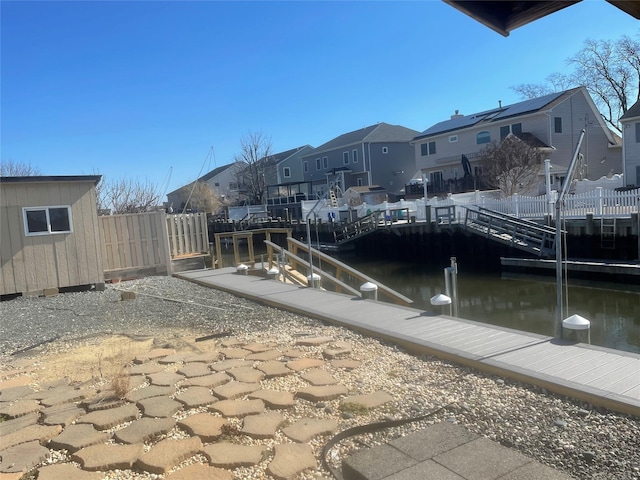 view of dock featuring a water view, fence, and a residential view