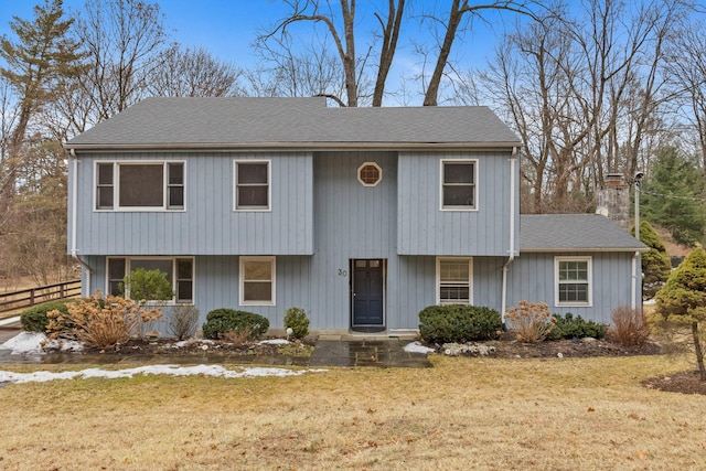 view of front facade featuring a shingled roof, a front yard, and fence