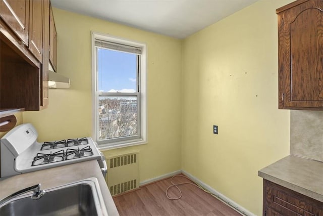 kitchen featuring a sink, light countertops, light wood-type flooring, radiator, and gas range gas stove