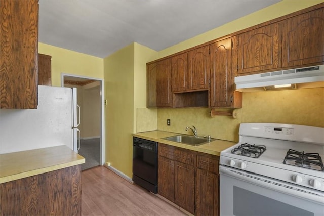 kitchen with white appliances, light wood-style flooring, light countertops, under cabinet range hood, and a sink