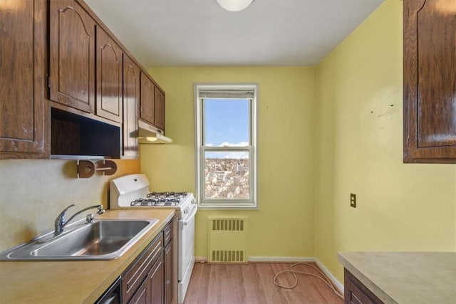 kitchen featuring white gas range, light countertops, light wood-style flooring, a sink, and under cabinet range hood