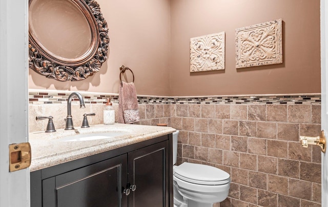 half bath featuring tile walls, wainscoting, vanity, and toilet