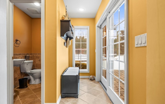 entryway with light tile patterned floors, a wainscoted wall, a wealth of natural light, and tile walls