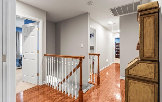 hallway featuring visible vents, attic access, light wood-style floors, an upstairs landing, and baseboards