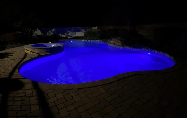 pool at night featuring a fenced in pool, a patio, and an in ground hot tub