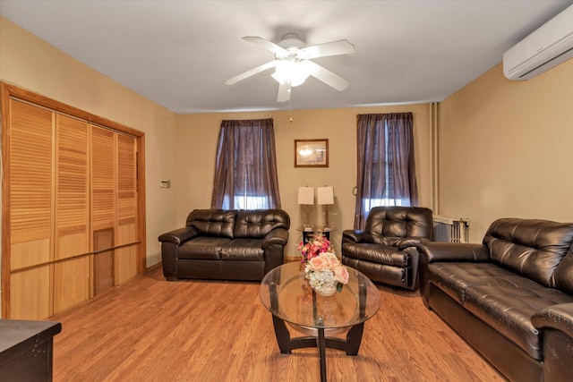 living area with an AC wall unit, a ceiling fan, and light wood-style floors