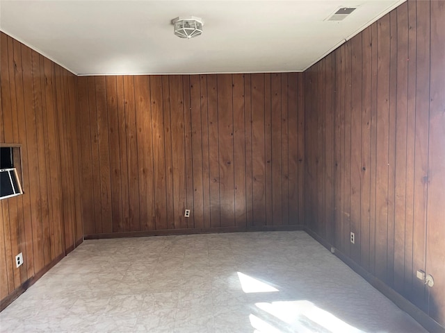 spare room with light floors, wood walls, visible vents, and baseboards