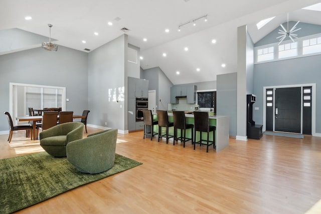 living area featuring light wood-style floors, baseboards, visible vents, and high vaulted ceiling