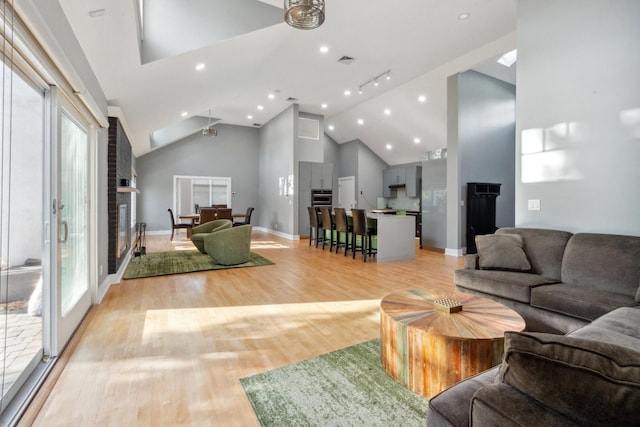 living room featuring high vaulted ceiling, visible vents, baseboards, light wood-style floors, and a glass covered fireplace