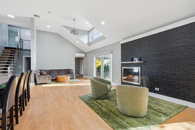 living area featuring light wood finished floors, visible vents, a brick fireplace, high vaulted ceiling, and stairs