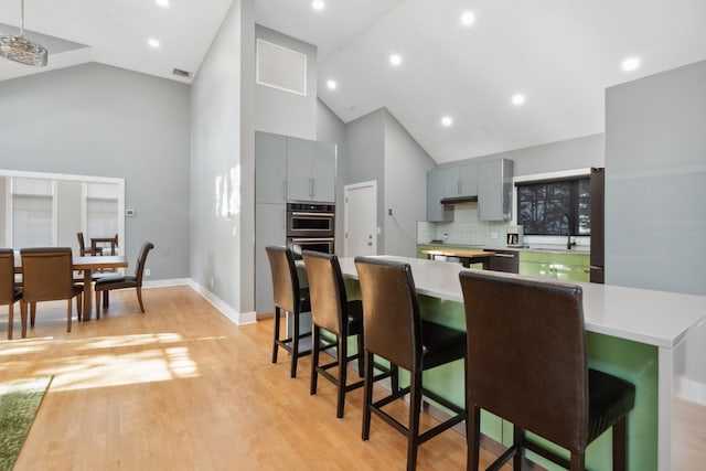 kitchen with a breakfast bar, tasteful backsplash, gray cabinetry, double oven, and light wood-type flooring