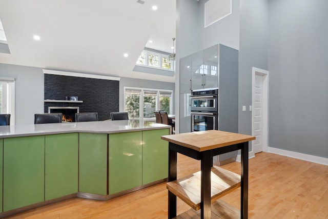 kitchen with light wood finished floors, light countertops, double oven, a fireplace, and green cabinetry