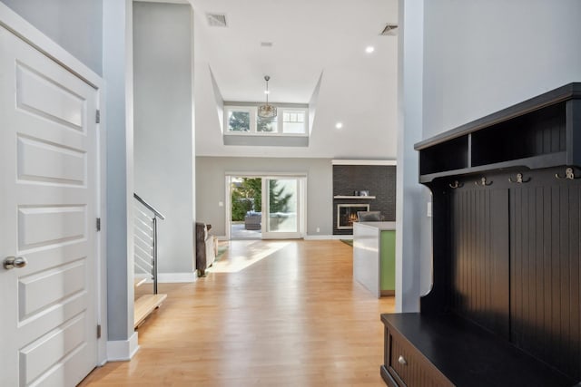 mudroom with visible vents, a towering ceiling, light wood-style floors, a brick fireplace, and baseboards