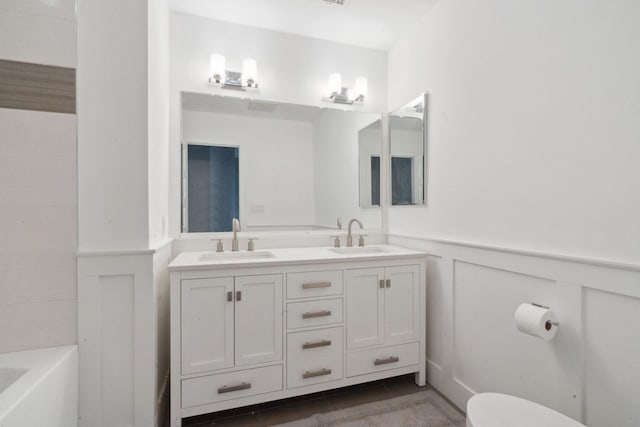 full bath featuring toilet, wainscoting, a sink, and a washtub