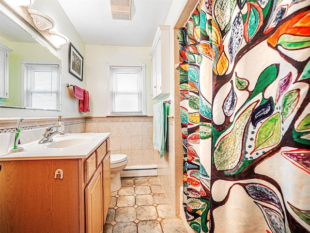 bathroom featuring a wealth of natural light, a wainscoted wall, tile walls, and toilet