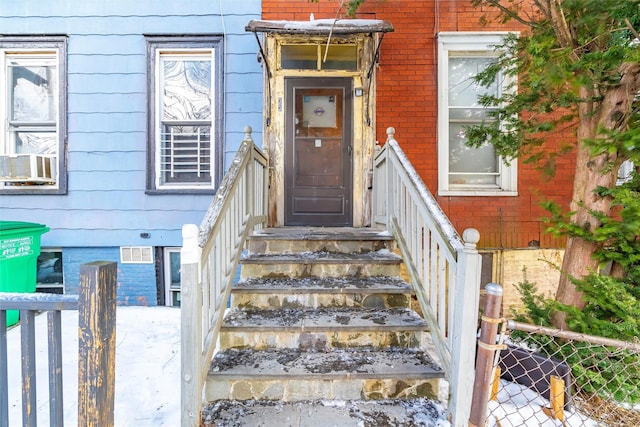 property entrance with visible vents, fence, and brick siding