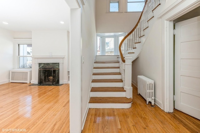 stairs featuring a high end fireplace, radiator, wood-type flooring, and baseboards