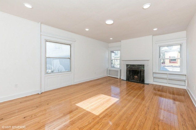 unfurnished living room featuring light wood finished floors, a premium fireplace, recessed lighting, and radiator