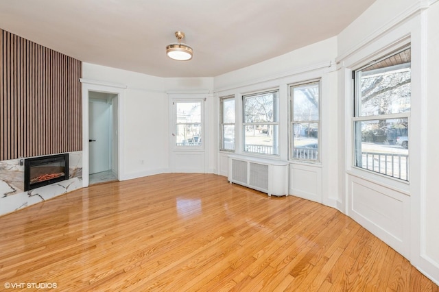 unfurnished living room featuring light wood-type flooring, radiator, and a premium fireplace