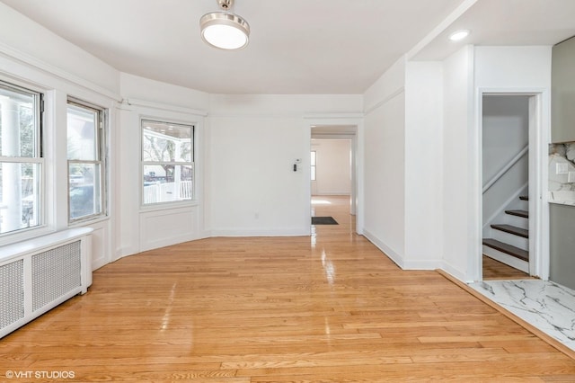 empty room with light wood-style floors, radiator, stairway, and baseboards