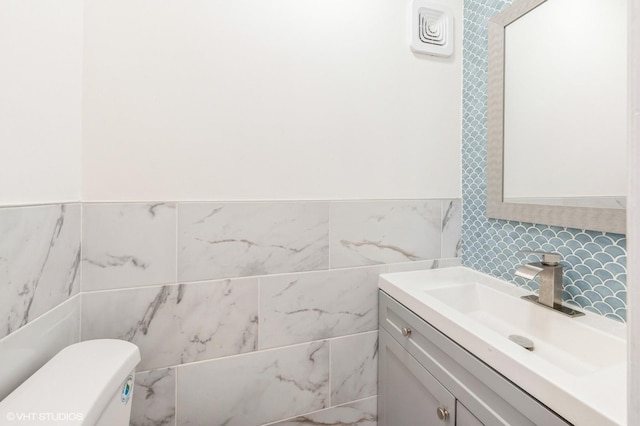 half bath featuring tile walls, vanity, and toilet