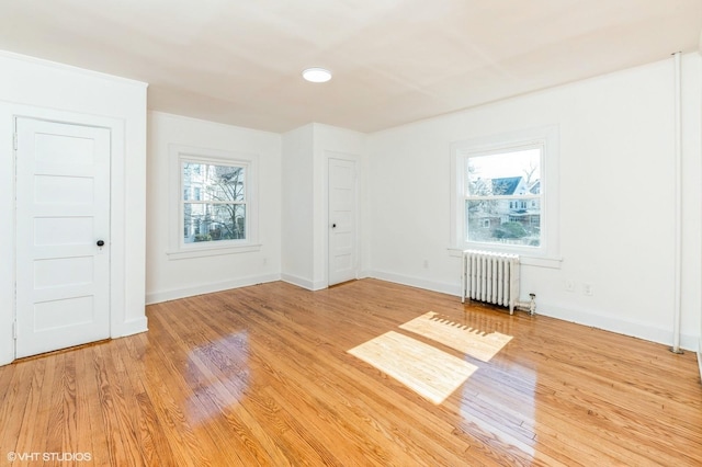 unfurnished room with baseboards, light wood-type flooring, a wealth of natural light, and radiator