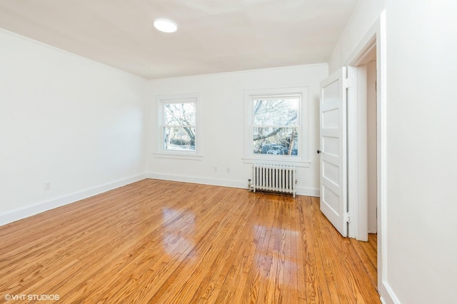 empty room featuring baseboards, light wood-type flooring, and radiator