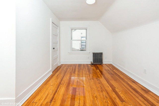 additional living space with baseboards, vaulted ceiling, radiator heating unit, and wood finished floors