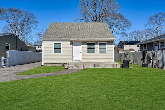 rear view of property featuring roof with shingles, fence, and a lawn