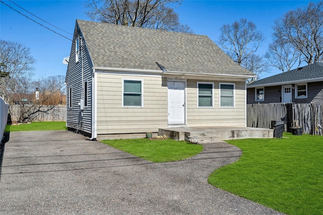 view of front facade with a shingled roof, a front yard, fence, and a patio