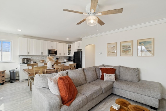 living room featuring ornamental molding, arched walkways, light wood-style flooring, and a ceiling fan