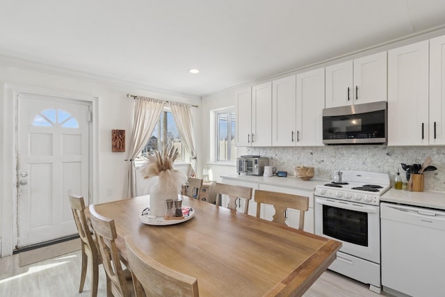 kitchen with white appliances, white cabinetry, light countertops, and backsplash