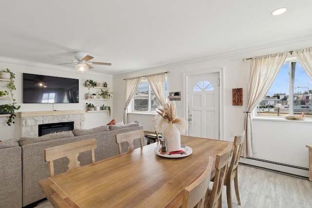 dining space with light wood finished floors, a ceiling fan, a baseboard radiator, ornamental molding, and a fireplace