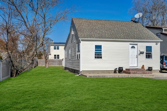 rear view of house with fence, a lawn, and roof with shingles