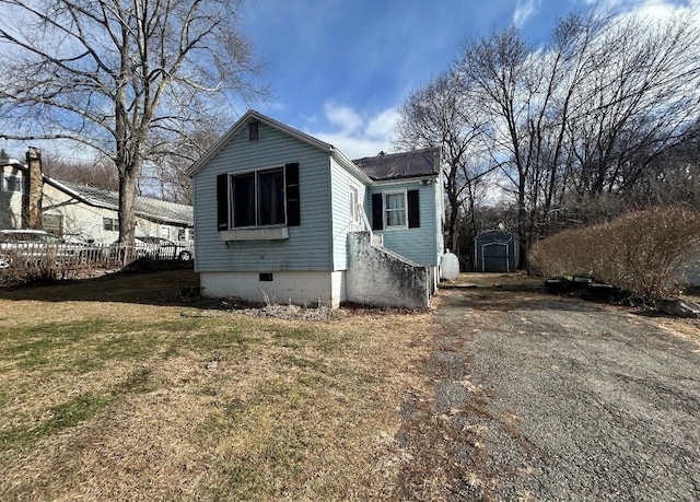 bungalow-style house featuring an outbuilding, crawl space, fence, a shed, and a front lawn