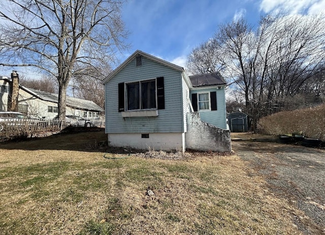 exterior space featuring an outbuilding, crawl space, fence, a shed, and a front lawn