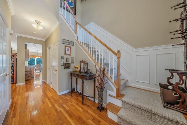 staircase with ornamental molding, hardwood / wood-style floors, baseboards, and a decorative wall